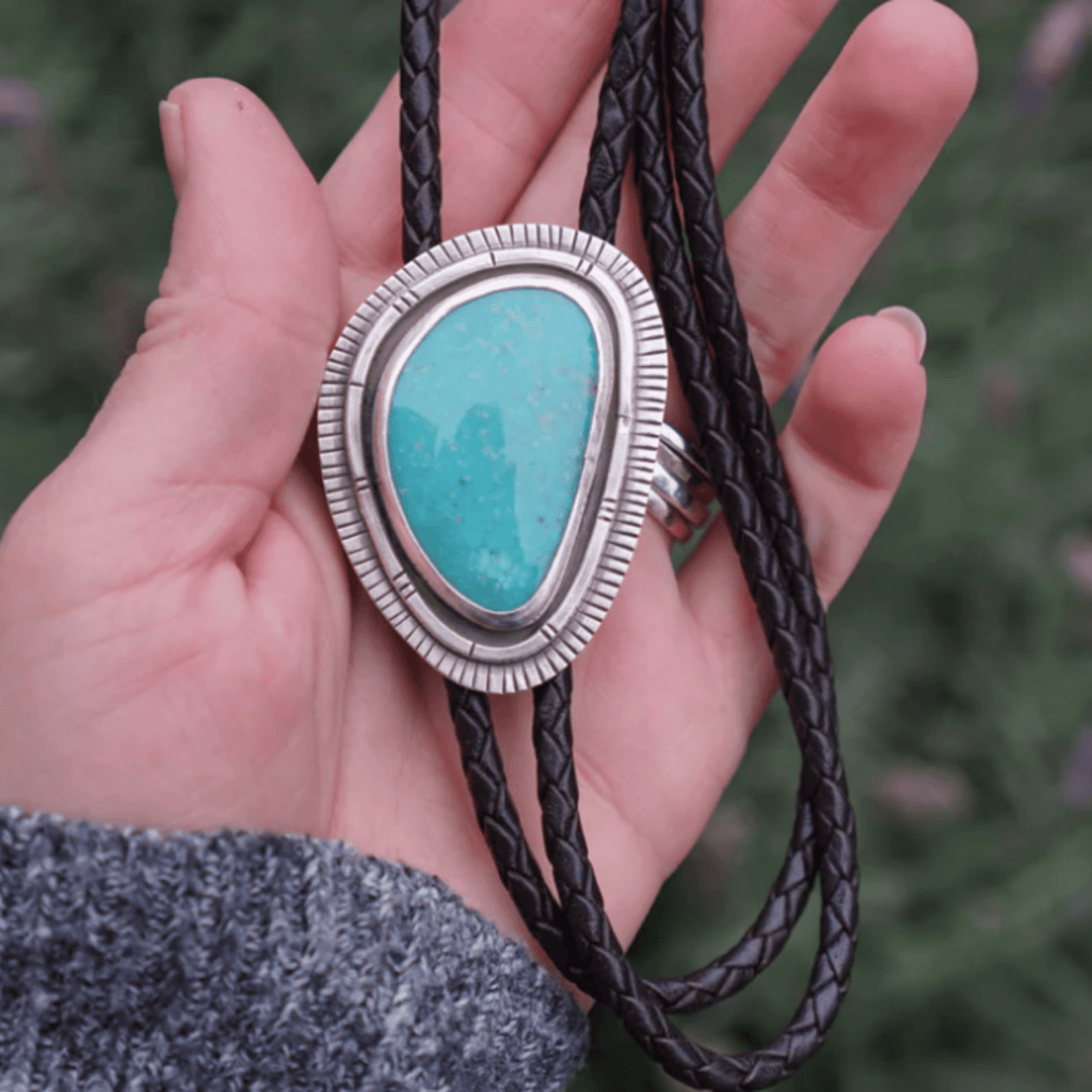 This Western Bolo Tie encorporates a large Turquoise stone set in layers of silver. Hand stamped for extra detail and oxidized and polished for a soft rustic finish. This bolo features a tension clasp and dark brown braided leather cord and finished with 